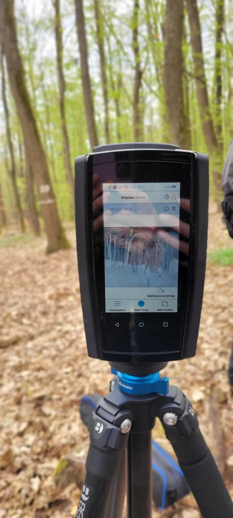 Terrestrial Laser Scanning (TLS) in a forest, with the device’s display showing a black-and-white scan of the forest.